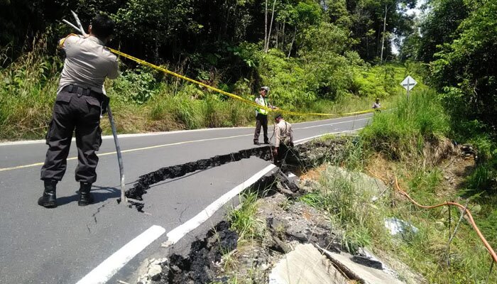 Petugas memasang garis polisi dijalan yang longsor.