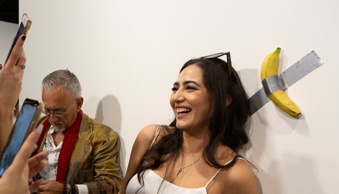 Seorang wanita berfoto di depan pisang yang dilakban, karya seni Maurizio Cattelan yang dipamerkan dalam dalam Art Basel 2019. (reuters)